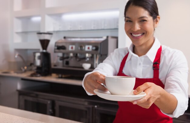 Giovane barista felice che offre tazza di caffè che sorride alla macchina fotografica