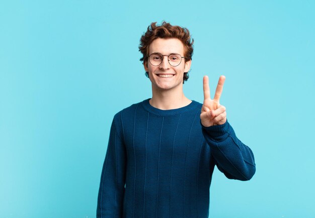 Giovane bel ragazzo che sorride e sembra felice, spensierato e positivo, gesticolando vittoria o pace con una mano