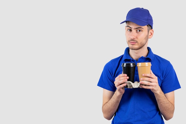 Giovane bel ragazzo in uniforme blu che dà l'ordine di caffè da asporto