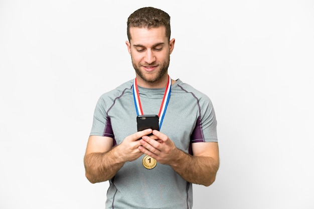 Giovane bell'uomo biondo con medaglie su sfondo bianco isolato inviando un messaggio con il cellulare