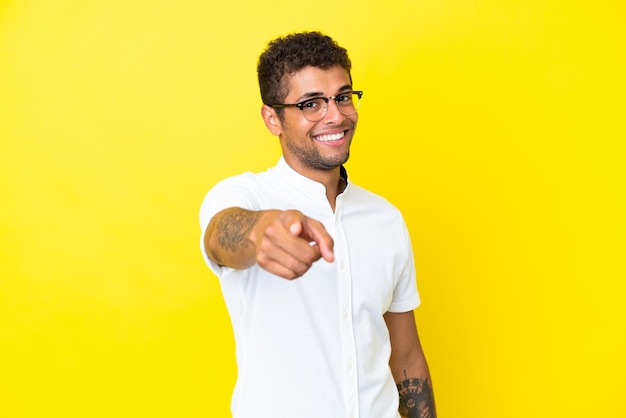 Giovane bell'uomo brasiliano isolato su sfondo giallo che punta davanti con espressione felice
