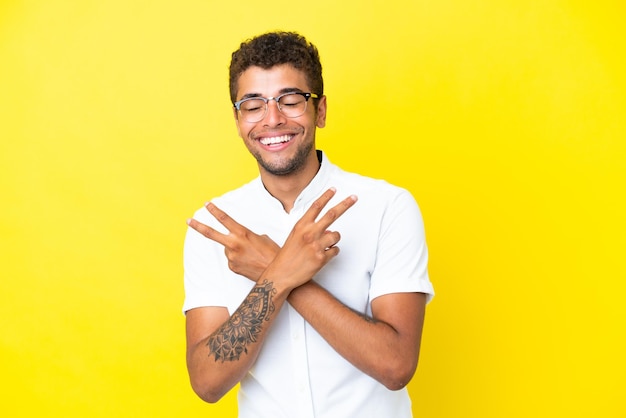 Giovane bell'uomo brasiliano isolato su sfondo giallo che sorride e mostra il segno della vittoria