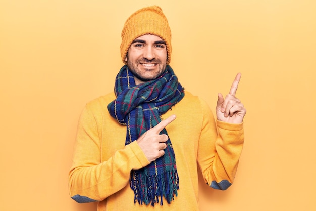 Giovane bell'uomo calvo che indossa abiti invernali sorridendo e guardando la telecamera che punta con due mani e dita di lato