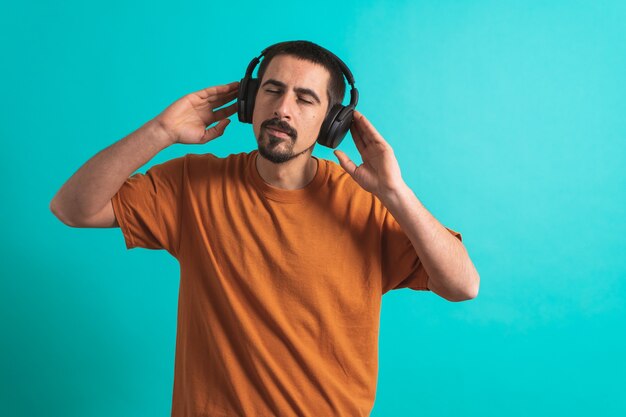 Giovane bell'uomo che balla e canta canzoni ascoltando musica in cuffia su sfondo blu