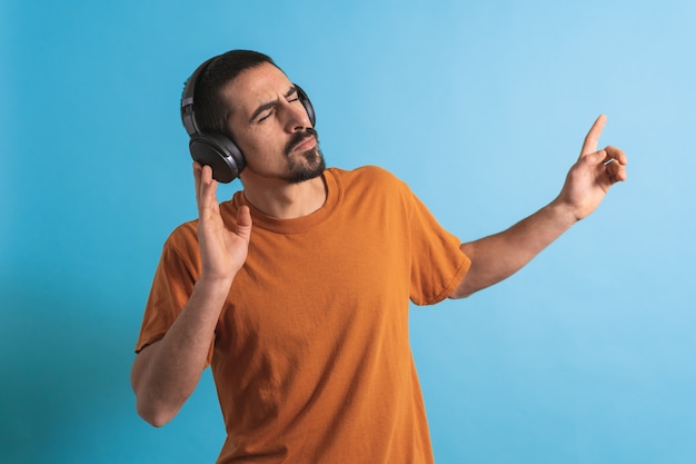 Giovane bell'uomo che balla e canta canzoni ascoltando musica in cuffia su sfondo blu