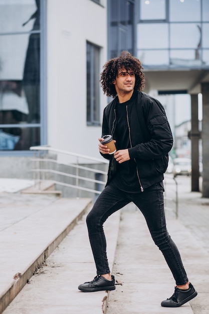Giovane bell'uomo che beve caffè e cammina per strada