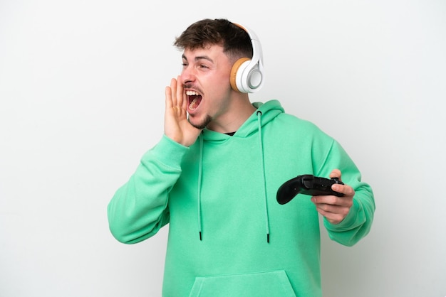Giovane bell'uomo che gioca con un controller per videogiochi isolato su sfondo bianco che grida con la bocca spalancata di lato