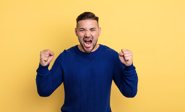 Giovane bell'uomo che grida in modo aggressivo con un'espressione arrabbiata o con i pugni chiusi celebrando il successo