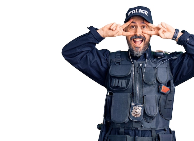 Giovane bell'uomo che indossa l'uniforme della polizia che fa il simbolo della pace con le dita sul viso sorridente allegro mostrando vittoria