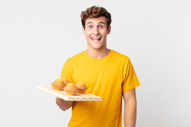 Giovane bell'uomo che sembra felice e piacevolmente sorpreso con in mano un vassoio di muffin