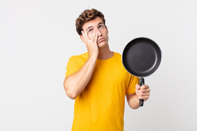 Giovane bell'uomo che si sente annoiato, frustrato e assonnato dopo una noiosa e con in mano una padella da cucina