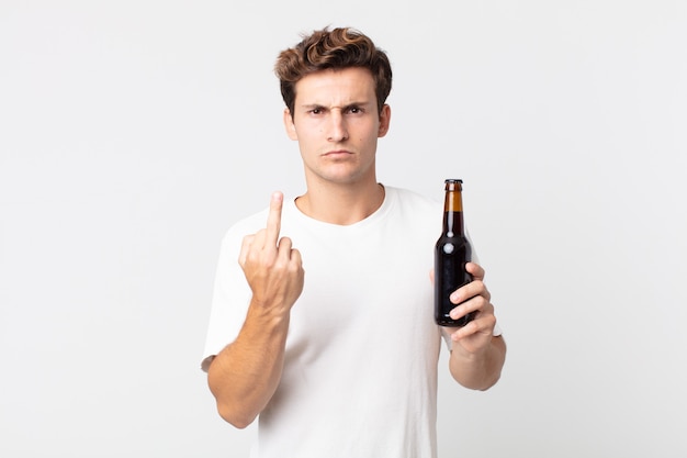 Giovane bell'uomo che si sente arrabbiato, infastidito, ribelle e aggressivo e tiene in mano una bottiglia di birra