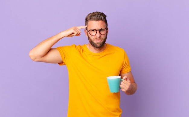 Giovane bell'uomo che si sente confuso e perplesso, mostrando che sei pazzo. e con in mano una tazza di caffè