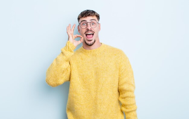 Giovane bell'uomo che si sente soddisfatto e soddisfatto, sorridente con la bocca spalancata, facendo segno bene con la mano