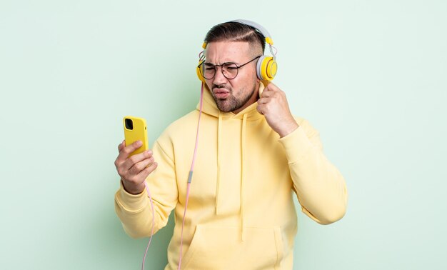 Giovane bell'uomo che si sente stressato, ansioso, stanco e frustrato. concetto di cuffie e smartphone