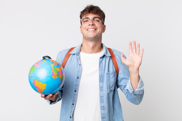 Giovane bell'uomo che sorride felicemente, agitando la mano, accogliendoti e salutandoti. studente con in mano una mappa del globo