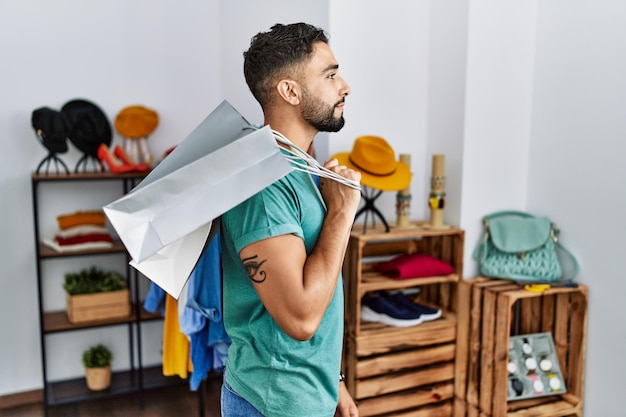 Giovane bell'uomo con la barba che tiene le borse della spesa al negozio al dettaglio che guarda al profilo di relax laterale posa con viso naturale e sorriso fiducioso