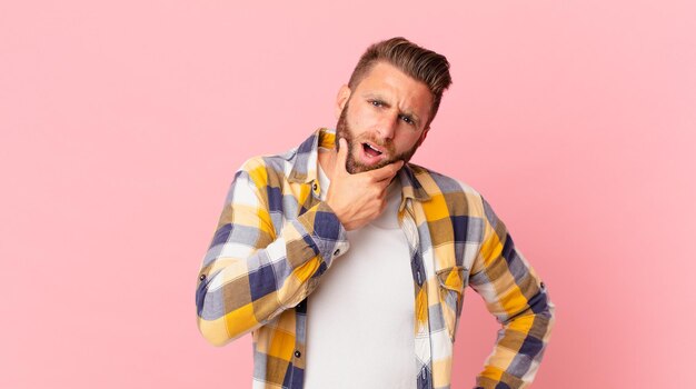 Giovane bell'uomo con la bocca e gli occhi spalancati e la mano sul mento