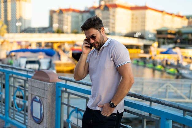 Giovane bell'uomo in maglietta polo classica che chiacchiera al telefono per strada bello fiducioso ed elegante