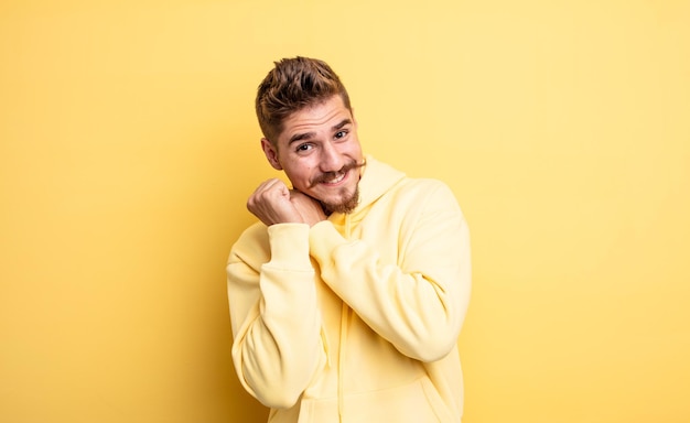 giovane bell'uomo innamorato e dall'aspetto carino, adorabile e felice, sorridente romanticamente con le mani accanto al viso. strano concetto di baffi