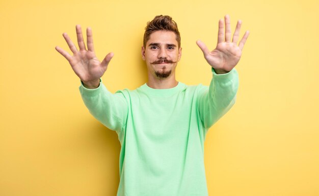 Giovane bell'uomo sorridente e dall'aspetto amichevole, che mostra il numero dieci o decimo con la mano in avanti, il conto alla rovescia. strano concetto di baffi