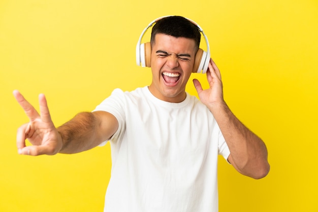 Giovane bell'uomo su sfondo giallo isolato ascoltando musica e cantando