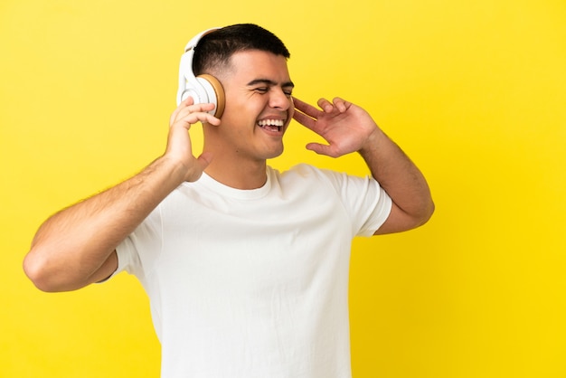 Giovane bell'uomo su sfondo giallo isolato ascoltando musica e cantando