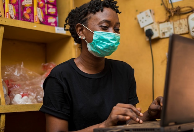 Giovane bella assistente africana che indossa una maschera facciale al supermercato mentre sta azionando il sistema