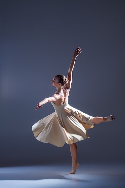 Giovane bella ballerina in abito beige che balla su sfondo grigio studio