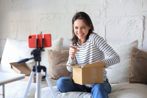 Giovane bella blogger femminile che registra video mentre disimballa il pacco a casa.