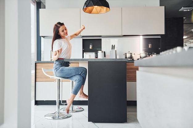 Giovane bella bruna in abiti casual si siede in cucina con una bevanda fresca al mattino