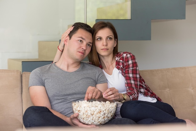 giovane bella coppia che si gode il tempo libero guardando la televisione con popcorn nella loro lussuosa villa di casa