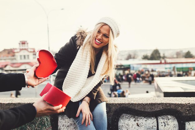 Giovane bella coppia che si gode una passeggiata in città a San Valentino. Il ragazzo fa un regalo alla sua ragazza.