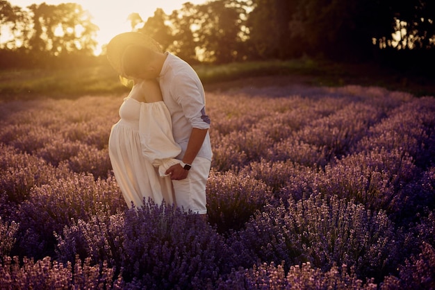 Giovane bella coppia incinta che cammina su un campo di lavanda al tramonto Concetto di famiglia felice