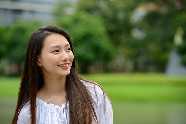 Giovane bella donna adolescente asiatica felice che pensa al parco