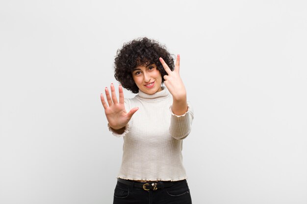 Giovane bella donna afro che sorride e che sembra amichevole, mostrando numero sette o settimo con la mano in avanti, il conto alla rovescia