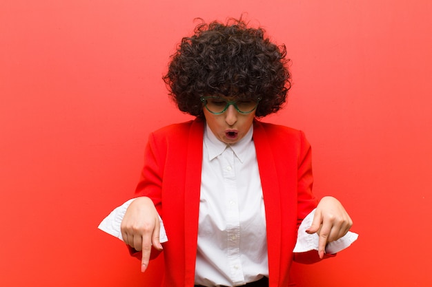 Giovane bella donna afro sentirsi scioccata, a bocca aperta e stupita, guardando e indicando verso il basso incredula e sorpresa