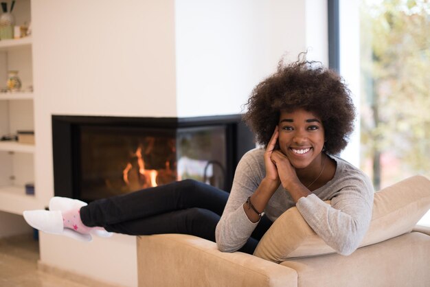 Giovane bella donna afroamericana che si rilassa sulla sedia davanti al camino al giorno d'autunno