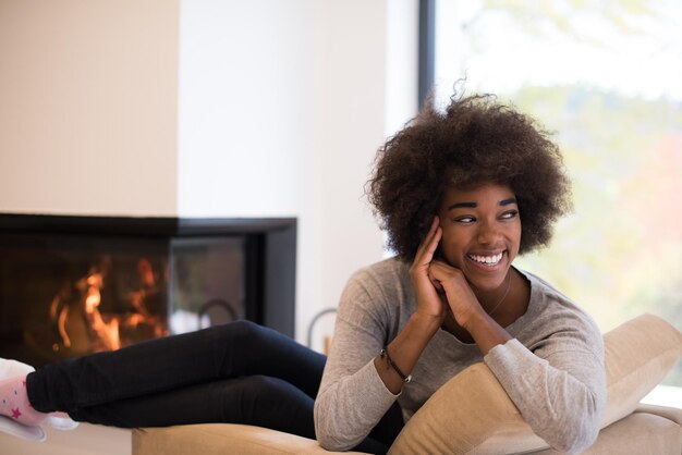 Giovane bella donna afroamericana che si rilassa sulla sedia davanti al camino al giorno d'autunno