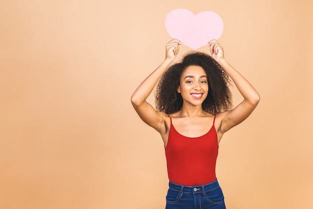 Giovane bella donna afroamericana che tiene un cuore rosa