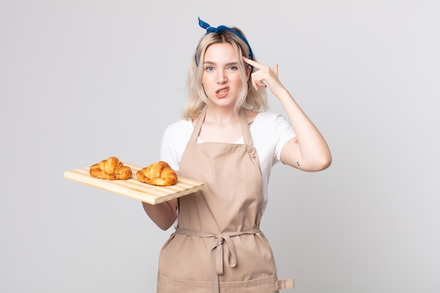 giovane bella donna albina che si sente confusa e perplessa, mostrando che sei pazzo con un vassoio di croissant