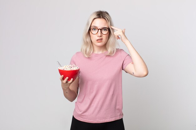 Giovane bella donna albina che si sente confusa e perplessa, mostrando che sei pazzo con una ciotola per la colazione