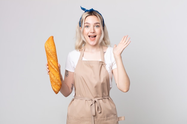 Giovane bella donna albina che si sente felice e stupita per qualcosa di incredibile con una baguette di pane