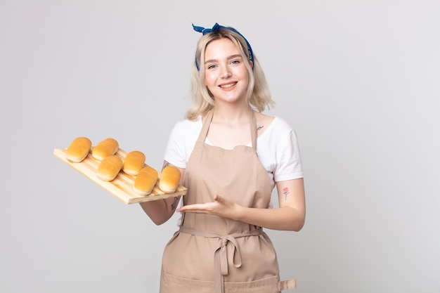 giovane bella donna albina che sorride allegramente, si sente felice e mostra un concetto con un vassoio di focacce di pane