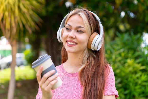 Giovane bella donna all'aperto che ascolta musica e tiene in mano un caffè da asporto