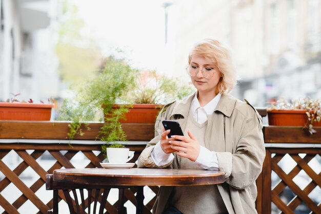 Giovane bella donna alla moda che si siede nel caffè della città in strada