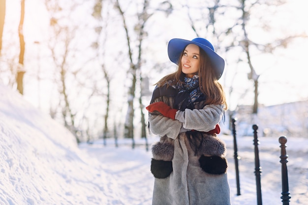 Giovane bella donna alla moda con il sorriso perfetto in cappello blu e sciarpa che cammina per strada