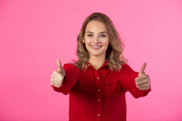 giovane bella donna allegra in abbigliamento rosso su un muro rosa con un gesto delle mani