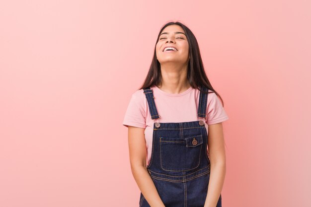 Giovane bella donna araba che indossa una salopette di jeans rilassata e felice ridendo, collo allungato mostrando i denti.