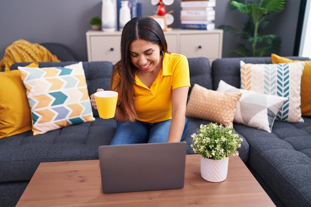 Giovane bella donna araba che usa il computer portatile che beve caffè a casa